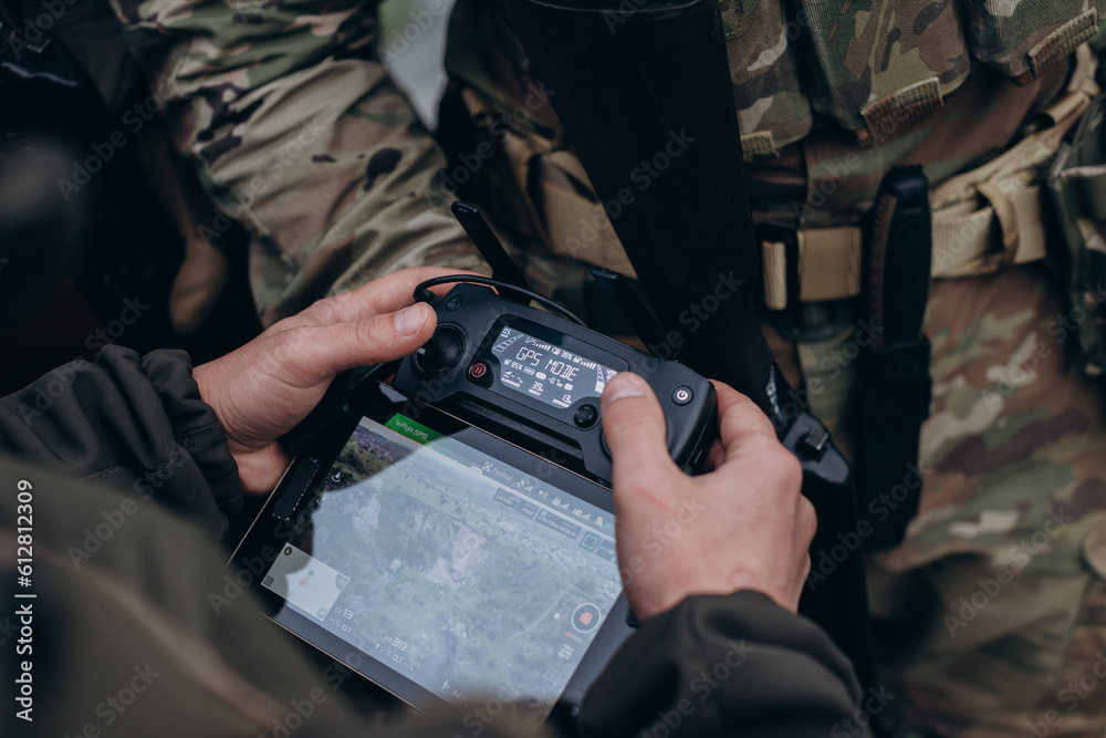 Two service members in camouflage operating a ruggedised ground control unit and map tablet in the field.